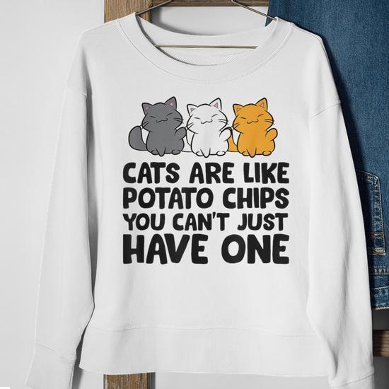 A white sweatshirt featuring three cartoon cats and the text, "CATS ARE LIKE POTATO CHIPS YOU CAN'T JUST HAVE ONE."